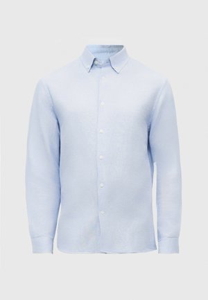 Camisa de manga larga azul claro con cuello puntiagudo y botones blancos sobre un fondo liso.