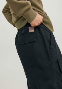 Pantaloni cargo neri con una vestibilità rilassata, caratterizzati da una tasca con patta, elastico in vita e un'etichetta in tessuto sul retro.