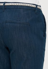 Námořnické modré kalhoty z denimu, s úzkým střihem, tkaným páskem s bílými akcenty a jednou zadní kapsou.