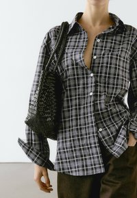 Koszula w czarno-białą kratę z zapięciem na guziki, w oversize'owym kroju i z podwiniętymi rękawami. Połączona z fakturowaną, czarną, plecioną torbą.