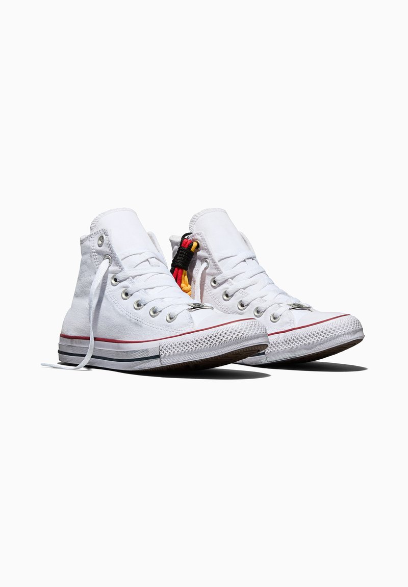 Pair of white high-top canvas sneakers with red and black stripes on soles, white laces, and a small multicolored cord detail on one shoe.