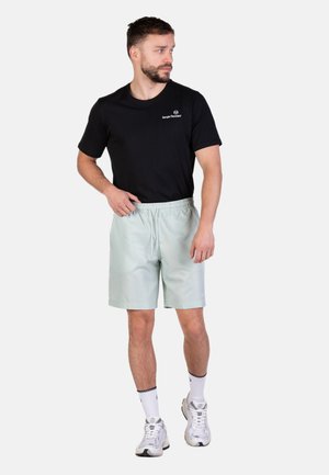 Hellgrüne Shorts mit elastischem Bund und Seitentaschen, kombiniert mit einem schwarzen Kurzarmshirt und weißen Sportschuhen.
