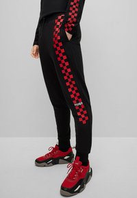 Czarne dresy z czerwonymi, w kratkę bocznymi paskami i logo "HUGO". Połączone z czerwono-czarnymi, masywnymi sneakerami. Miękka tkanina i elastyczny pas.