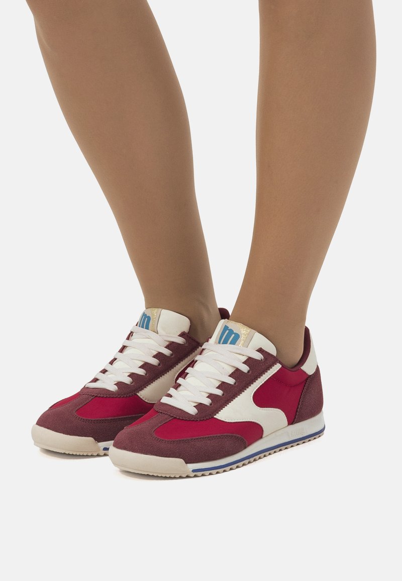 Rote und weiße Wildledersneaker mit niedriger Profilhöhe, ausgestattet mit weißen Schnürsenkeln, einem blauen Logo auf der Zunge und einer strukturierten Gummisohle.
