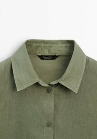 Chemise en lin vert olive à col avec boutons sur le devant, étiquette visible à l'intérieur du col portant l'inscription « Massimo Dutti Made in Portugal ».