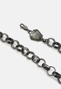 Juodas metalinis grandinys su persipynusiais ovaliais ir apvaliais žiedais, su šešiakampio akmens detale ir vėžlio užsegimu.