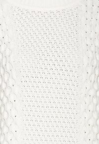 Pull blanc en maille avec motif ajouré central et détails en torsades sur les côtés.