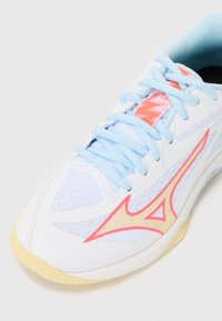 White athletic shoe with light blue laces and accents, featuring a pink logo and textured material. Soft yellow sole.