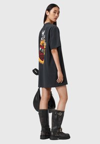 Czarny oversize t-shirt z kolorową grafiką na plecach. Modelka nosi czarne kozaki do kolan i trzyma czarną torbę.