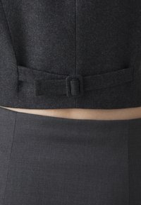 Dunkelgraue, maßgeschneiderte Stoffweste mit quadratischem Design, ausgestattet mit einer Schleifen-Detail auf der Rückseite und einem passenden, enganliegenden grauen Rock. Glatte Textur.