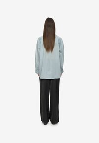 Light blue vertically striped oversized shirt with long sleeves, paired with black wide-leg pants. The shirt has a buttoned cuff detail.