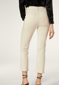 Beige slim-fit kalhoty se středně vysokým pasem, s zadními kapsami a zkráceným lemem. Vyrobeny z hladké tkaniny s jemným elastickým efektem.