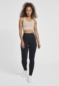 Beige ribbad sportbh med breda axelband, kombinerad med högmidjade svarta leggings med texturdetaljer, båda bar tillsammans med vita sneakers.