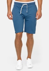Blauwe katoenen shorts met een trekkoord in de taille, omgeslagen zomen, zijzakken en een aansluitende snit, gecombineerd met witte sneakers.