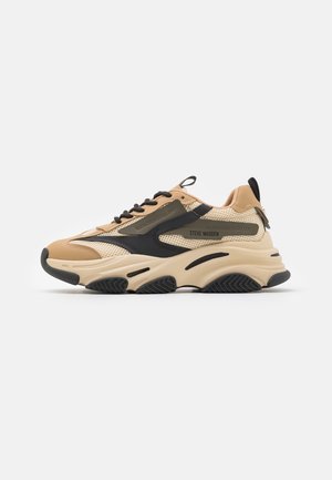 Sneaker Steve Madden beige e nera, chunky, con tomaia in mesh e pelle, suola spessa e scolpita, e lacci neri, vista laterale.