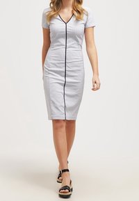 Šedé pruhované pouzdrové šaty s krátkými rukávy, výstřihem do V, černým lemováním vpředu a sukní po kolena. Kombinované s černými sandály na platformě.