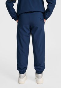 Mörkblå joggers med elastiska mudd och midja, tillverkade av ett texturerat tyg. Har en avslappnad passform och bärs med ljusa sneakers.