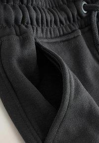 Schwarze Jogginghose mit elastischem Bund, Kordelzug und seitlicher Tasche. Weicher Baumwollstoff mit glatter Oberfläche und sichtbaren Nähten.