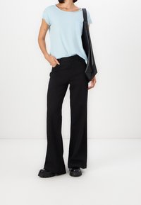 Světle modré tričko s krátkým rukávem a kapsou, kombinované s černými širšími kalhotami a masivními černými platformovými botami, doplněné černou taškou.