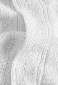 Weißer Strickstoff mit einem strukturierten Muster, das erhabene Stiche und eine glatte, weiche Oberfläche aufweist.