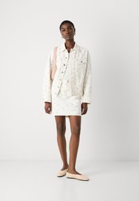 Veste en denim blanche avec des motifs floraux roses, jupe assortie et ballerines beiges. Tissu léger et coupe classique avec des fermetures à boutons.