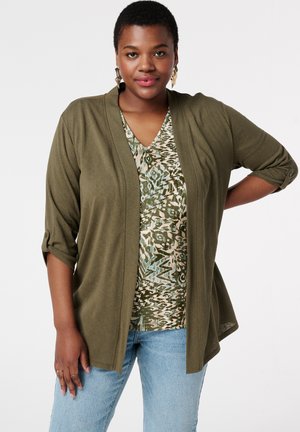 Olijfgroen cardigan met driekwartmouwen over een gestreepte top in groen, beige en blauw. Lichtblauwe jeans maken de outfit af.
