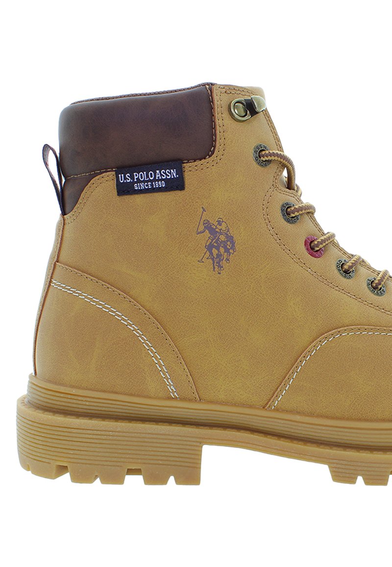 Bottines de randonnée à lacets beige avec un col rembourré marron, semelle en caoutchouc épaisse, étiquette U.S. Polo Assn. et logo de joueur de polo sur le côté.