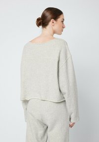 Sweatshirt court gris clair en tissu doux avec une coupe décontractée, un col large, des épaules tombantes et des coutures visibles au bas.