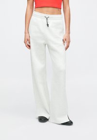 Ανοιχτό γκρι, φαρδύ παντελόνι φόρμας με σούρα στη μέση και πλαϊνές σκισμές, φτιαγμένο από μαλακό ύφασμα. Διαθέτει μικρό λογότυπο στο μπροστινό μέρος.