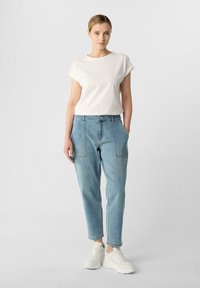 Witte katoenen t-shirt met opgerolde mouwen, gecombineerd met lichtblauwe denim jeans met voorzakken, gedragen met witte sneakers.