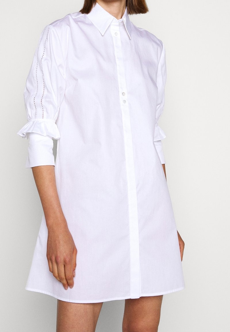 Abito bianco a camicia con taglio dritto, caratterizzato da maniche a palloncino e dettagli arricciati ai polsini, realizzato in leggero cotone.