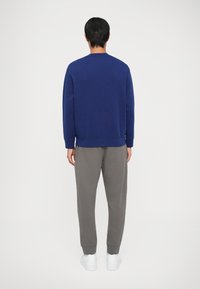 Felpa blu navy con maniche lunghe e scollatura tonda, abbinata a pantaloni della tuta grigi, con polsini e orlo a coste. Sneakers bianche sotto.