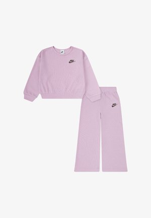 Completo Nike composto da maglia a maniche lunghe con collo tondo in maglia waffle lilla e pantaloni a gamba larga con logo Nike nero sul petto e sulla coscia sinistra.