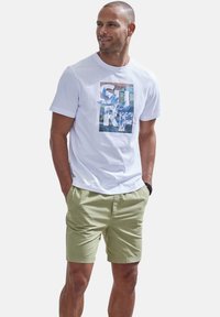 Weißes Baumwoll-T-Shirt mit buntem "SURF"-Grafik, kombiniert mit hellgrünen Shorts. Das T-Shirt hat einen Rundhalsausschnitt und kurze Ärmel.