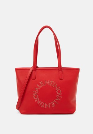 Red leather tote bag with dual handles and removable strap. Features studded logo design in a circular pattern on the front. Smooth texture.
