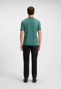 Men's short-sleeve t-shirt in teal, featuring a straight cut and crew neck. Paired with black jeans and sturdy black shoes.