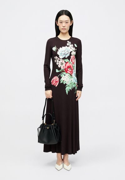 Kostim z dolgimi rokavi v temno rjavi barvi s cvetličnim vzorcem v rdeči in svetlo modri barvi. Model drži črno torbico v obliki vedra in nosi bele špičaste čevlje.