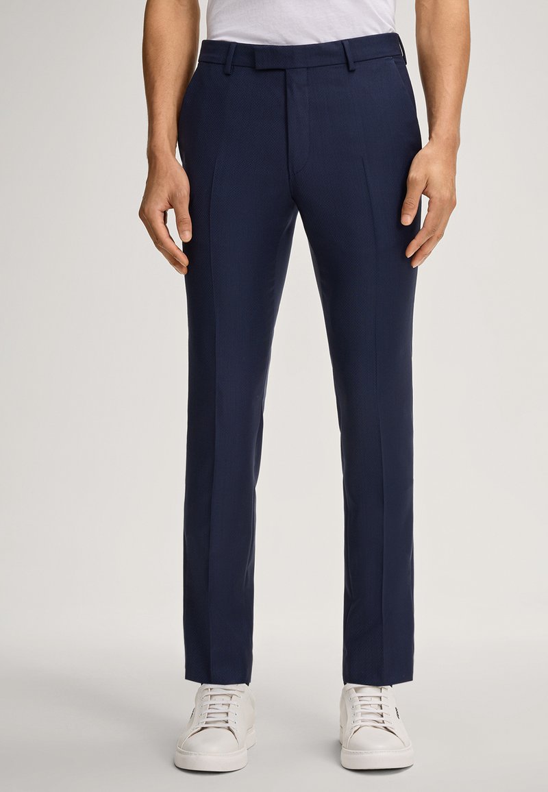Marineblaue maßgeschneiderte Hosen mit strukturiertem Oberflächen, zwei vorderen Falten und schmaler Passform. Kombiniert mit weißen Sneakers für einen lässigen Look.