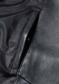 Poche de veste en cuir noir avec coutures visibles et tissu de doublure intérieure lisse de couleur sombre.