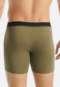 Oliivinvihreät bokserishortsit mustalla joustavalla vyötärönauhalla. Sileä pinta ja vartalonmyötäinen malli, jossa kontrastitikkaukset reunoissa.