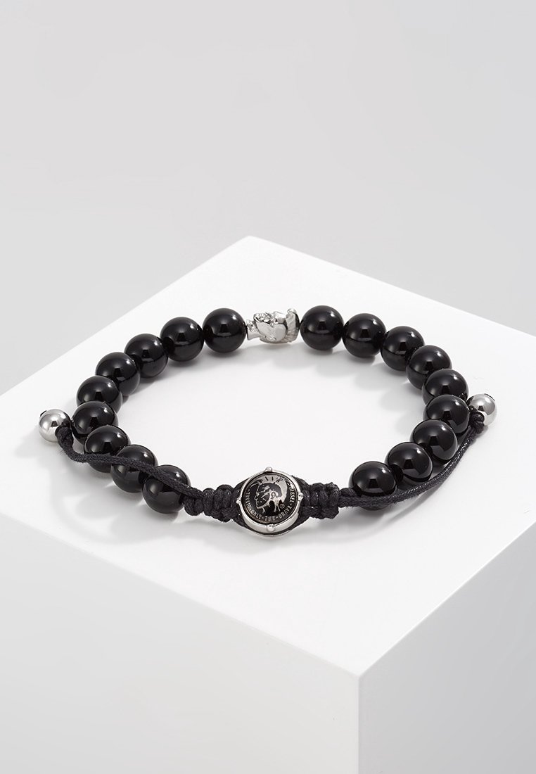 Bracelet noir en perles rondes, avec un emblème de lion en argent au centre, des accents de perles argentées et une fermeture réglable par cordon noir.