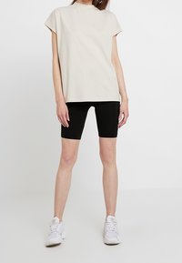 Vaahto beige-tyylinen oversized t-paita, jossa on lyhyet hihat, yhdistetty mustiin pyöräilyshortseihin ja valkoisiin urheilukenkään. Yksinkertainen, rento muotoilu.