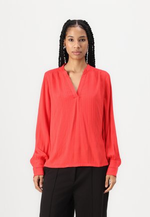 Chemisier rouge à manches longues avec un col en V, doté de rayures verticales et de poignets élastiques, fabriqué en tissu léger et texturé.