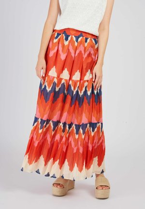 Woman wearing a long, tiered skirt with bold orange, pink, navy, and cream zigzag patterns and beige platform sandals.