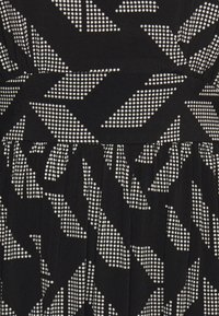 Vestido de tela negra con un patrón geométrico de puntos blancos y triángulos afilados; superficie texturizada con detalles plisados en el dobladillo.