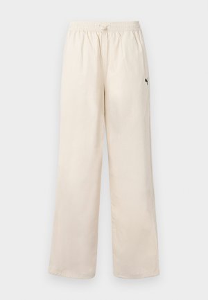 Pantalons larges beige clair avec une taille élastique et un cordon de serrage. Dotés d'un petit logo noir sur le côté. Texture lisse.