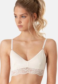 Bra morbido in crema con design a V, bordatura in pizzo sul fondo, spalline regolabili e finitura in tessuto liscia.
