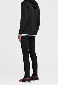 Svart huvtröja, slim fit svarta byxor och svarta sneakers med röda accenter. Slät tygkänsla, avslappnad design och minimal hårdvara.