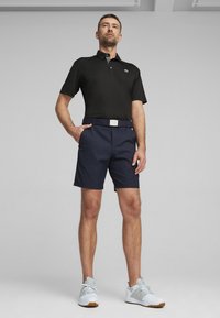 Čierne polo tričko so sivým golierom, námornícke šortky a modrý opasok so striebornou prackou. Svetlošedé atletické topánky s hnedými podešvami.