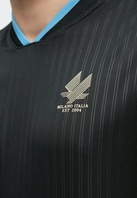 Melns sporta krekls ar vertikālām svītrām, zilu apkakli un zelta logo ar uzrakstu "Milano Italia EST 2004" uz krūtīm.